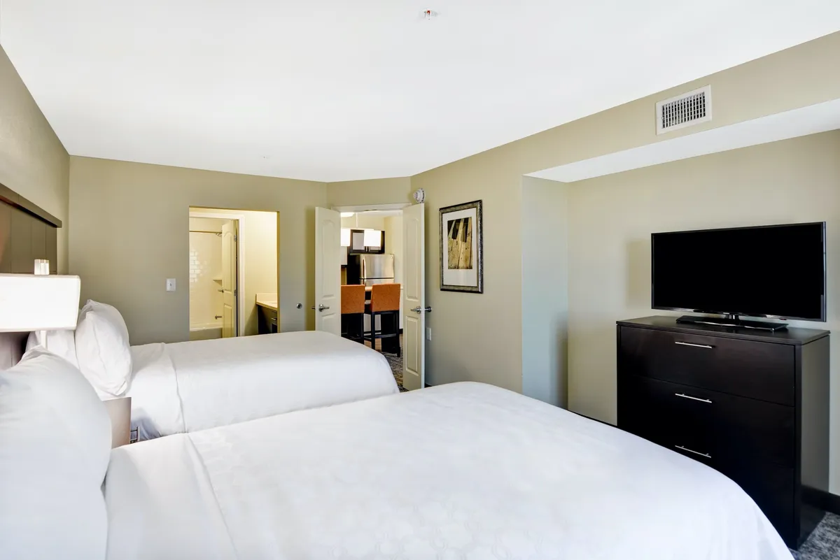 A private bedroom featuring two inviting double beds, a dresser, wall-mounted television, and tasteful artwork. The space is bathed in soft lighting, creating a cozy and comfortable atmosphere ideal for relaxing or unwinding after a busy day.