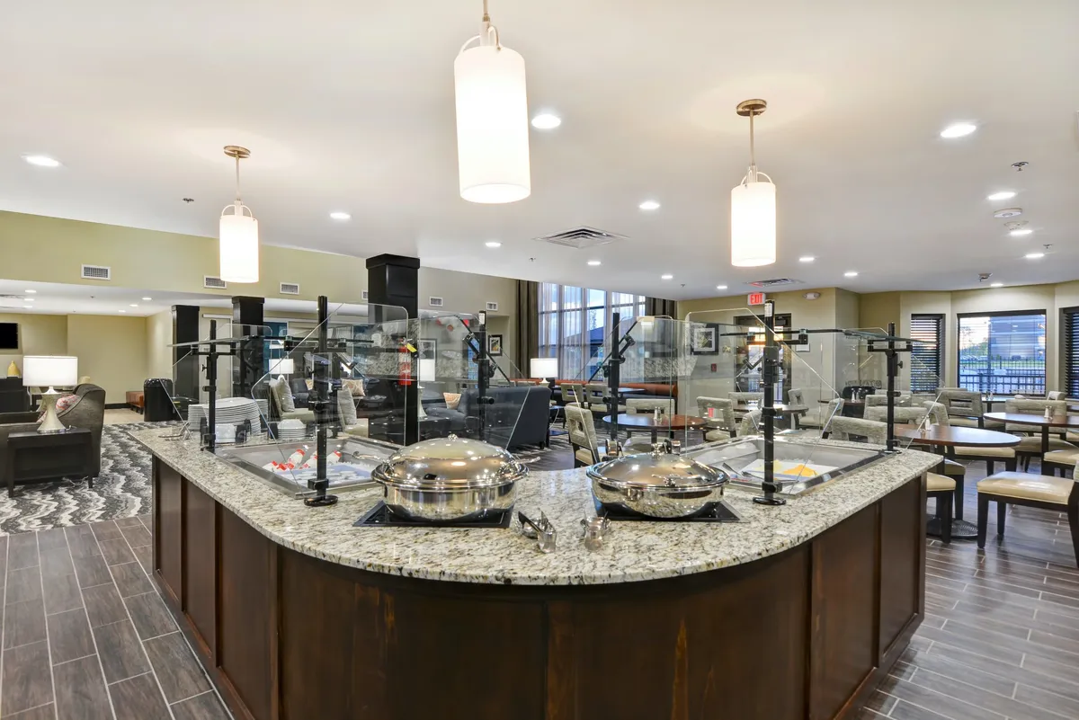 A bright, inviting communal dining space with granite countertops, serving stations, and modern lighting fixtures. The scene suggests shared meals, social interaction, and the flexibility to enjoy breakfast or host gatherings—an essential amenity for group travelers or longer visits.