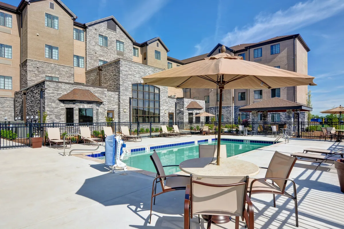 A vibrant exterior view of the seasonal outdoor swimming pool, surrounded by comfortable outdoor seating and umbrellas, with the property’s building facade in the background. The setting captures guests enjoying the pool, sunbathing, and relaxing in a lively yet tranquil atmosphere.