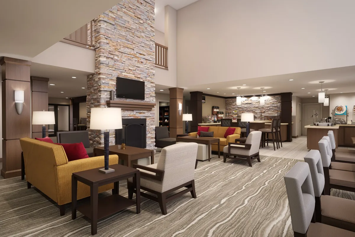 A welcoming lounge area with a stone fireplace serves as the focal point, surrounded by plush seating and bathed in natural light from large windows. The atmosphere is cozy and sociable, inviting guests to relax together after a day of exploring the city.