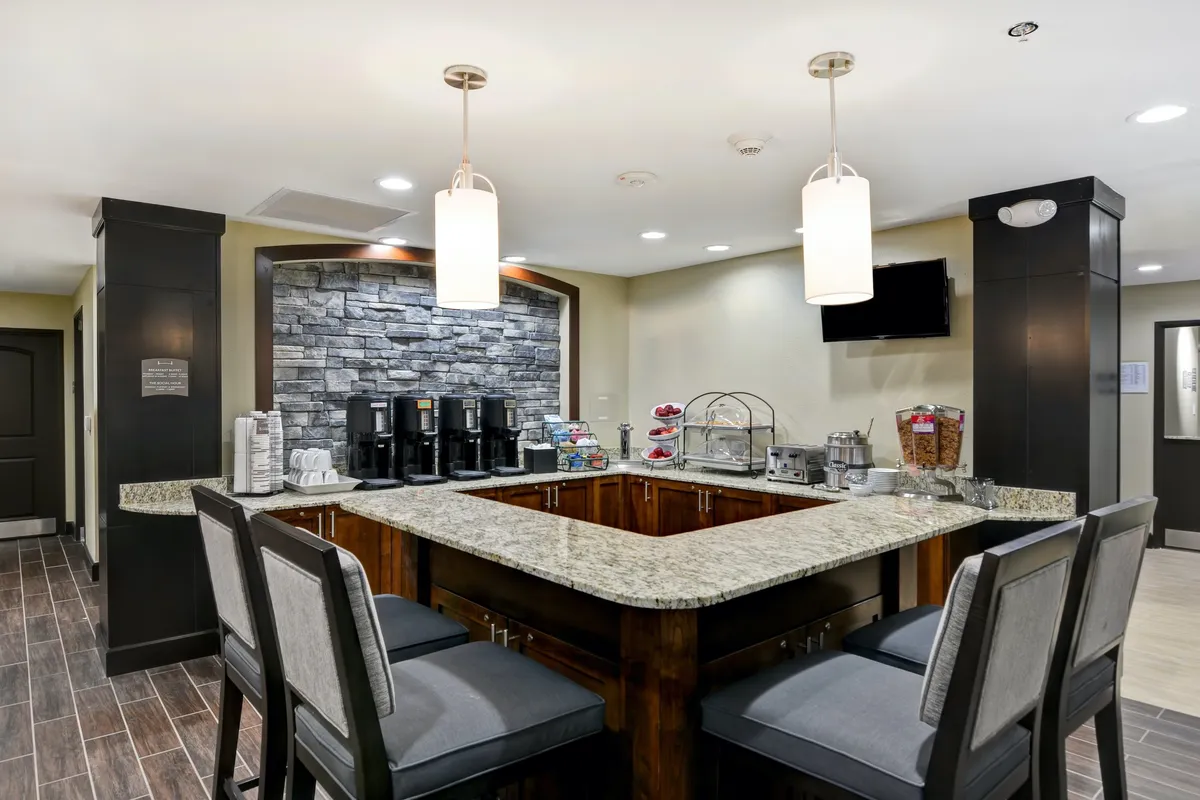 The image features a granite countertop coffee station with bar stools, a snack display, and a stylish stone accent wall. This inviting space is set up for enjoying morning coffee, grabbing snacks, or chatting with family and friends, echoing the homey, self-catering vibe emphasized in the section.