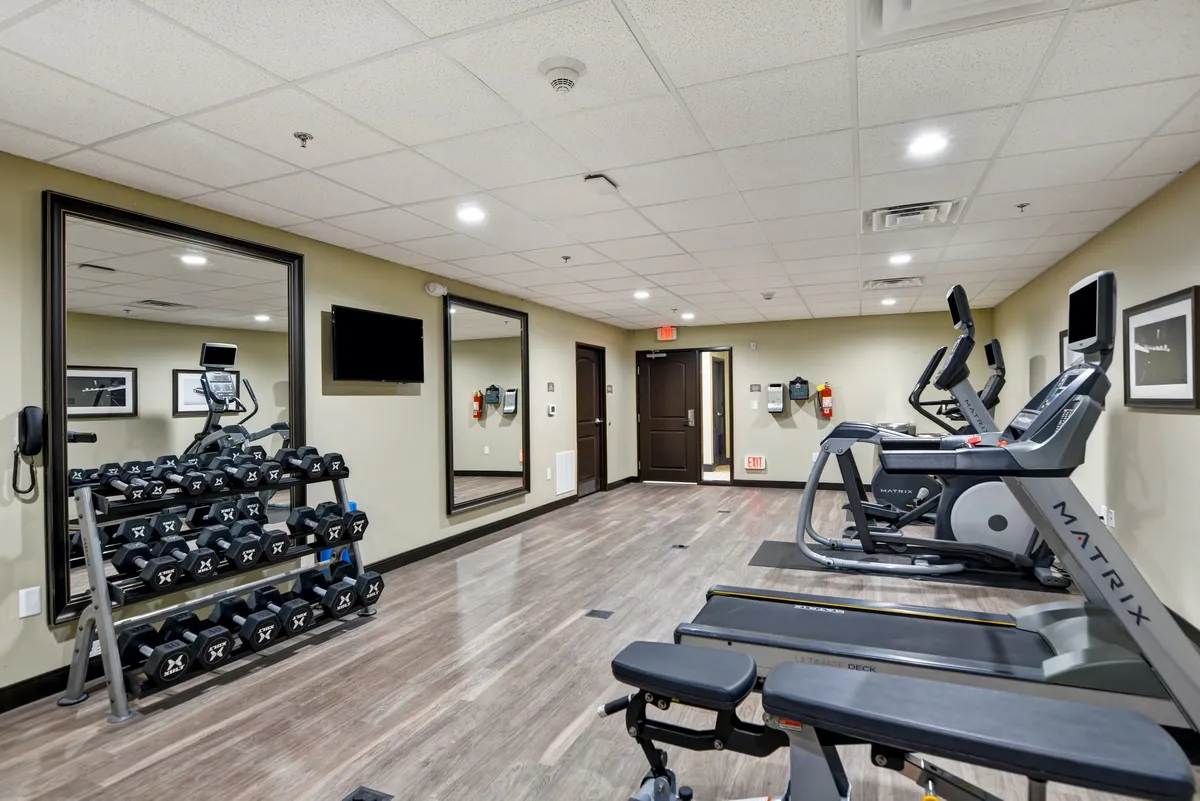 A modern fitness center equipped with a dumbbell rack, treadmill, and elliptical machine. The space exudes energy and motivation, inviting guests to keep up with their fitness routines while traveling.