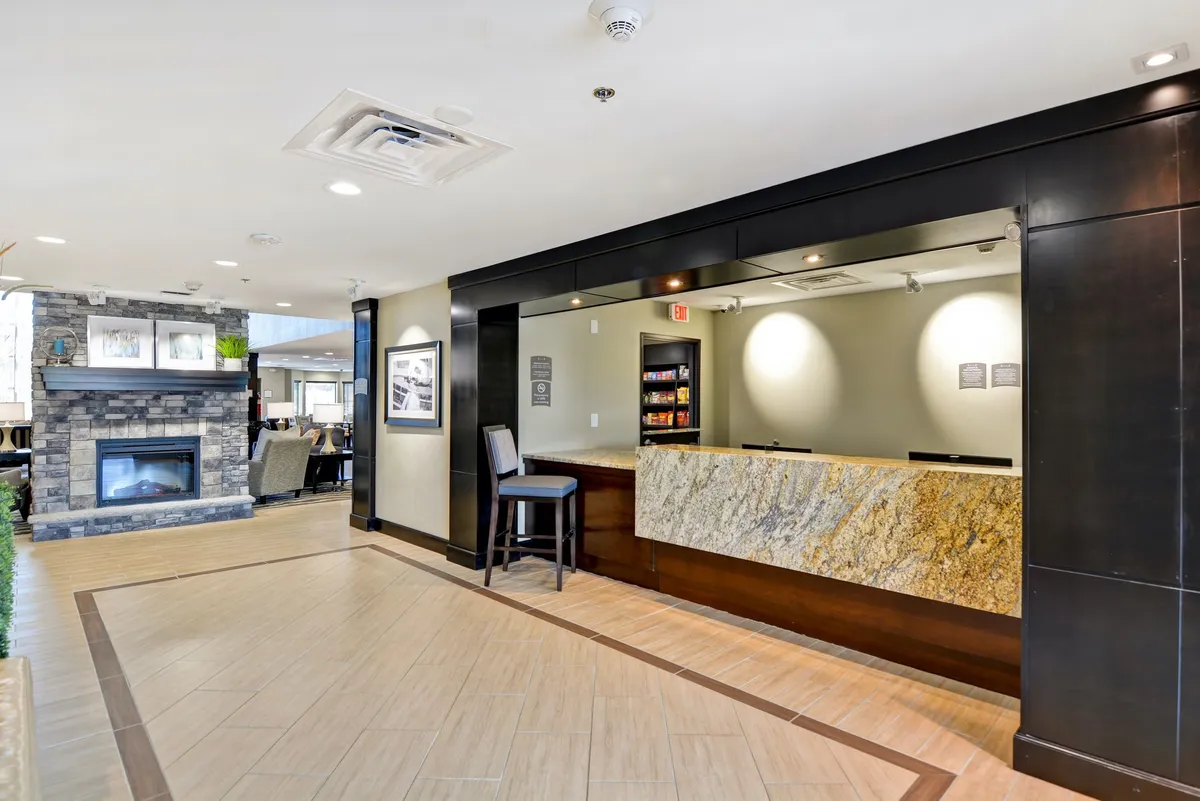 This image shows a welcoming reception desk area framed by a fireplace and comfortable seating, with guests either checking in or relaxing. The presence of staff and an inviting lounge setting immediately signals hotel amenities and a communal atmosphere, ideal for group arrivals and extended stays.