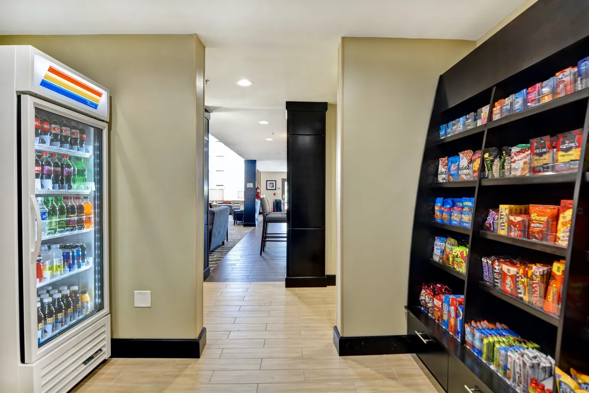 A casual hallway area featuring a well-stocked vending machine and snack shelf, with a glimpse toward a living space beyond. The scene suggests easy access to refreshments and communal moments, ideal for guests recharging between outings.