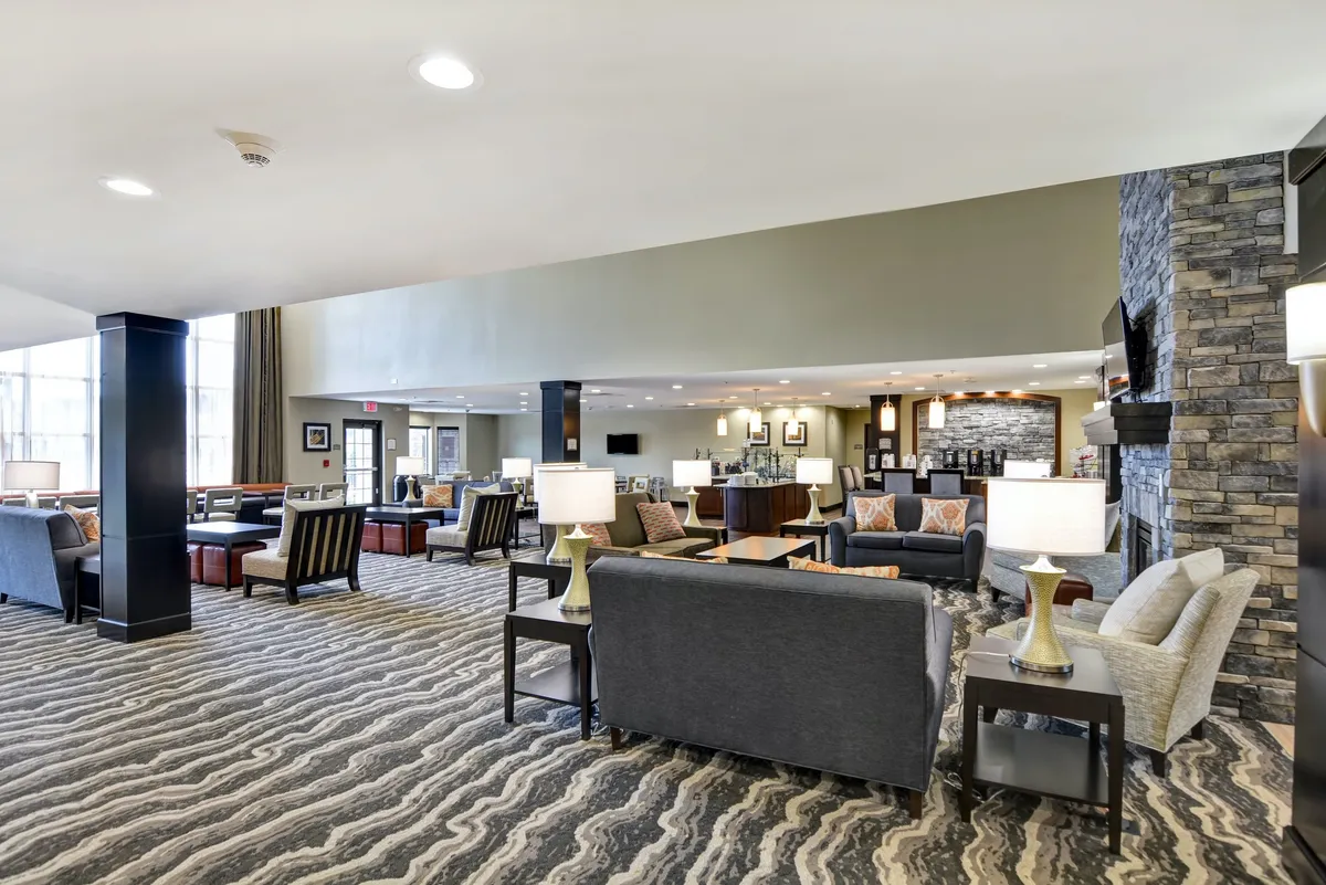 A spacious living area adorned with plush sofas and coffee tables, centered around a warm fireplace. The lighting fixtures create an inviting ambiance, and the arrangement of furniture encourages both relaxation and social interaction. The space is versatile, suitable for lounging, working, or gathering with others.