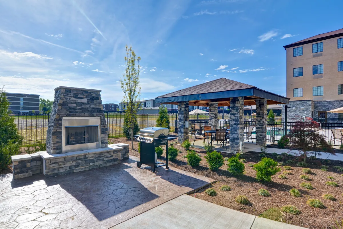 A well-maintained outdoor pavilion area, complete with a stone fireplace, grill, and landscaped garden. The space is ideal for barbecues, gatherings, and relaxed outdoor dining, set in a cheerful, social mood.
