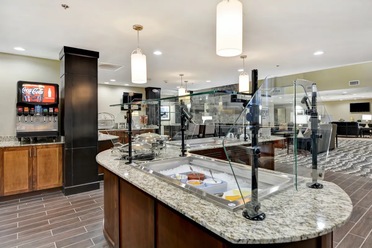 A modern food display area with a granite countertop and beverage station, designed for self-service dining and social gatherings. The bright and open setup evokes the convenience and flexibility of preparing or serving meals in a communal space.