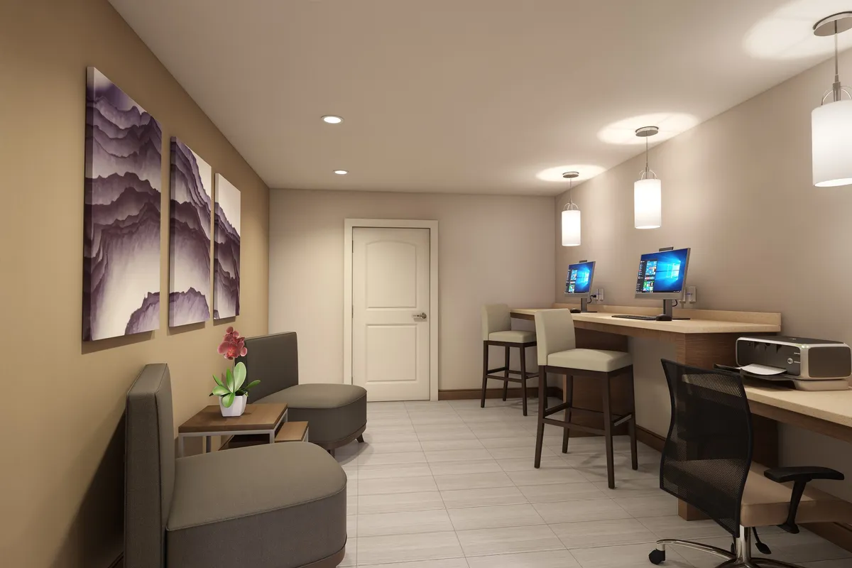 A comfortable, modern business center with workstations, computers, decorative artwork, and a cozy seating area with plants. The space feels productive yet inviting, supporting both focused work and creative projects.