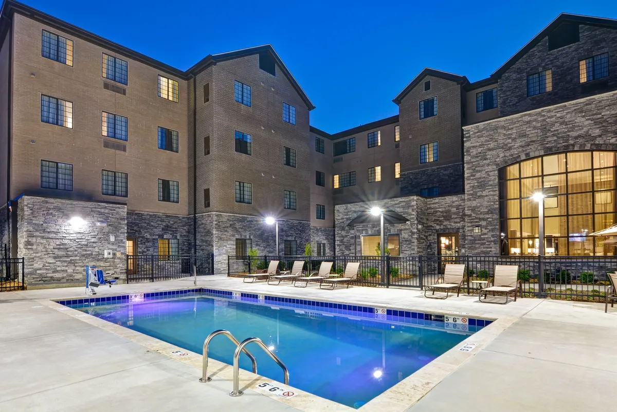 This image features a sparkling outdoor swimming pool with lounge chairs arranged around it, set against the backdrop of the property’s building facade. The relaxed mood is perfect for families wanting to unwind or play after a day of exploration.